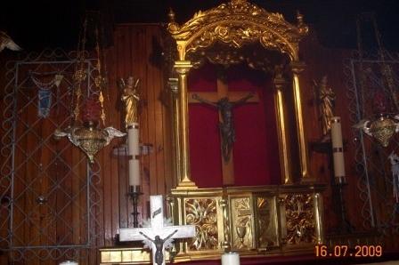 Wnętrze kościoła z okazałym ołtarzem, złotym krucyfiksem i białym krzyżem ze świecami.
