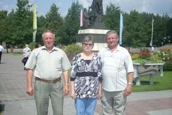 Grupa trzech uczestników wycieczki na tle pomnika, prawdopodobnie w Toruniu.