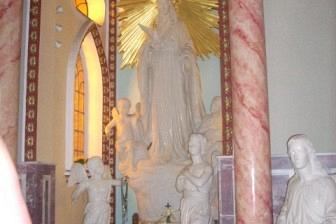 Biała figura sakralna w ozdobnej niszy kościoła, otoczona złotymi detalami.