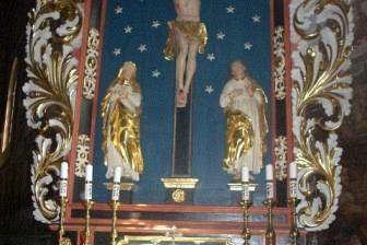 Bogato zdobiony ołtarz z krucyfiksem, figurami świętych i gwieździstym tłem.