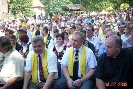 Uczestnicy Zjazdu Kaszubów w Bytowie siedzą na zewnątrz, wielu w żółtych szarfach.