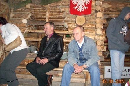 Grupa osób podczas wycieczki w drewnianym wnętrzu z polskim orłem na tle ściany.