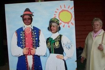 Kolorowy obraz pary w strojach kaszubskich, obok niewyraźny człowiek.