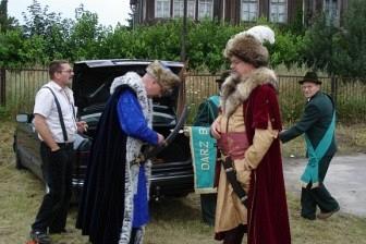 Kilka osób w regionalnych strojach podczas Zjazdu Kaszubów z domem w tle.