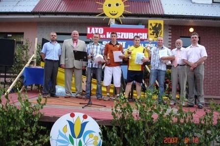 Zwycięzcy festynu sportowego na Kaszubach z nagrodami i pucharami na podium.
