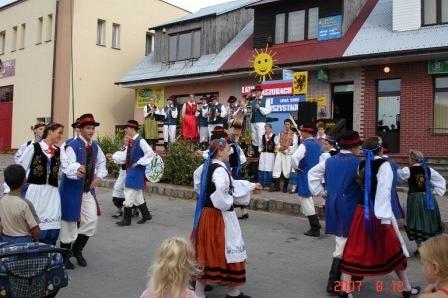 Grupa w tradycyjnych kaszubskich strojach ludowych tańczy podczas festynu na ulicy.