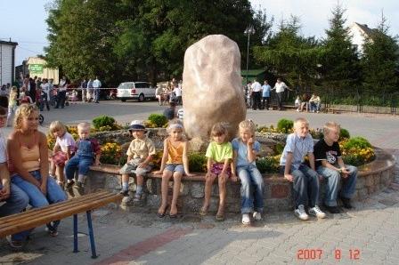 Uczestnicy festynu na Kaszubach siedzą wokół dużego kamienia, na świeżym powietrzu.