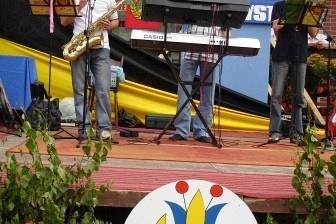 Okrągłe logo festynu na Kaszubach na tle barwnego wydarzenia sportowego.