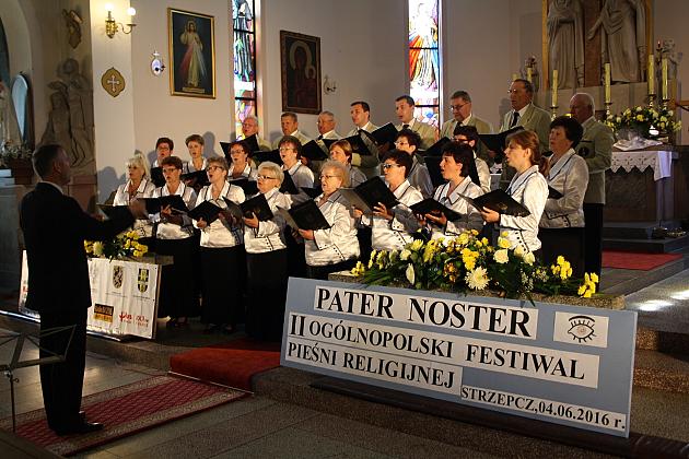 Chór w kościele za transparentem Pater Noster Strzepcz 2016, ozdobionym kwiatami, z dyrygentem.