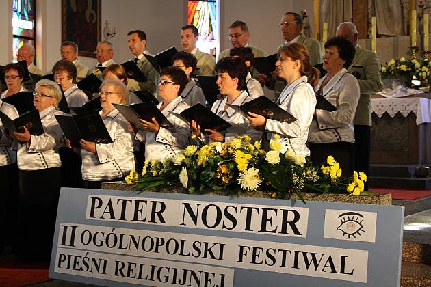 Chór śpiewający za stołem z napisem PATER NOSTER II Ogólnopolski Festiwal Pieśni Religijnej.