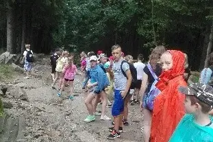 Uczestnicy kolonii w kolorowych płaszczach przeciwdeszczowych idą leśną ścieżką.