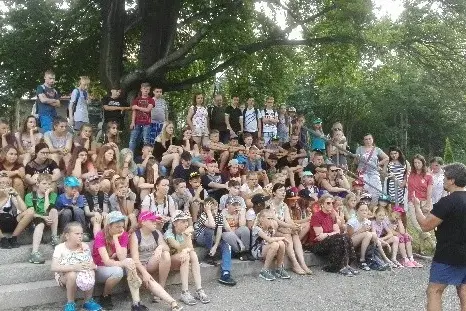 Uczestnicy kolonii językowej w Karpaczu pozują do zdjęcia, siedząc na zewnątrz wśród zieleni.