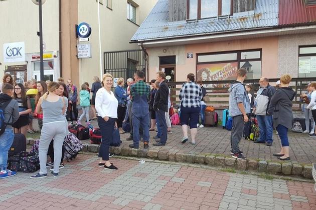 Grupa uczestników kolonii językowej stoi przed budynkiem w miejskim otoczeniu.