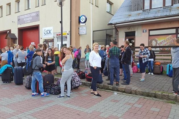 Uczestnicy kolonii z bagażami oczekują na zbiórce przed budynkami.