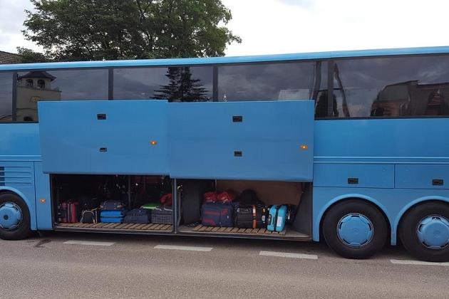 Błękitny autokar z otwartymi lukami bagażowymi, gotowy na wyjazd kolonijny.
