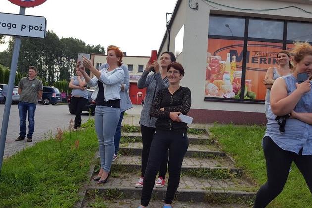 Uczestnicy kolonii stoją i idą na chodniku przy budynku, obok ulicy.