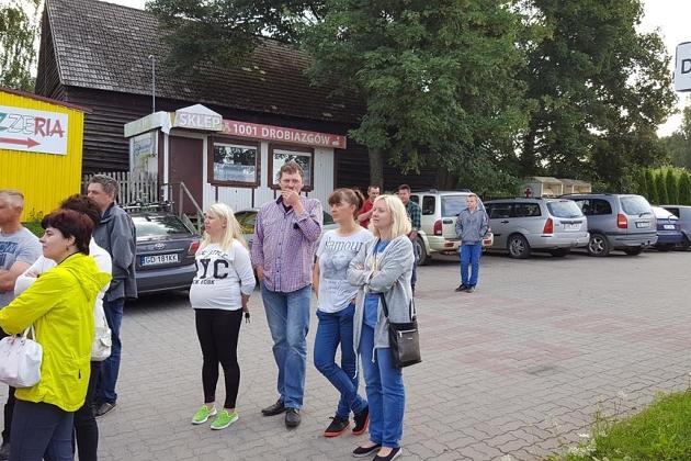 Uczestnicy kolonii językowej stojący na zewnątrz, obok budynków i zaparkowanych aut.