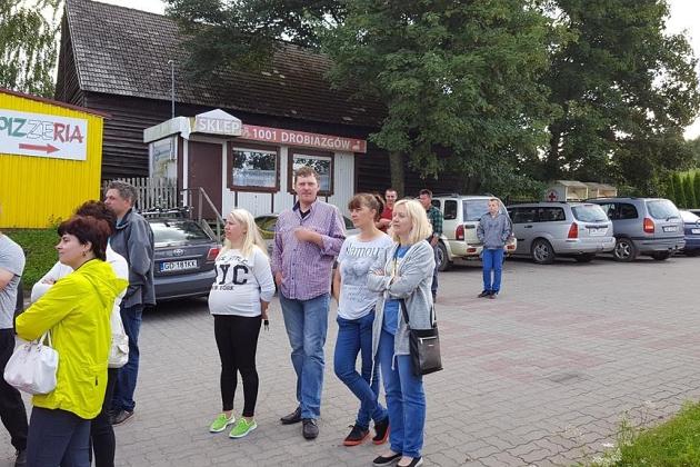 Uczestnicy kolonii językowej zebrani przed budynkiem, w tle parking i drzewa.