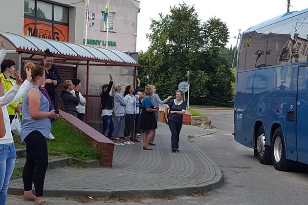 Koloniści z bagażami stoją przed niebieskim autobusem.