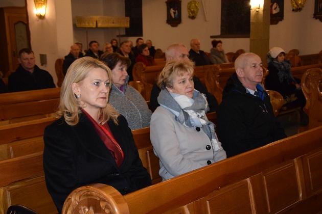 Uczestnicy spotkania gminnego koła pszczelarzy siedzą na drewnianych ławkach.