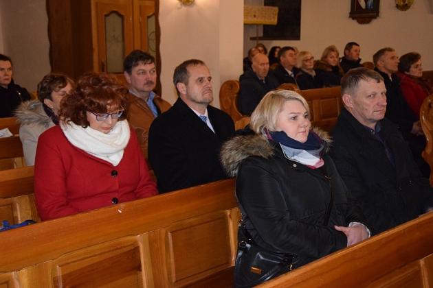 Uczestnicy świątecznego spotkania pszczelarzy siedzą w drewnianych ławkach.