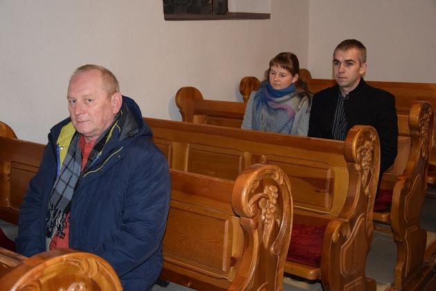 Uczestnicy spotkania siedzą na ozdobnych drewnianych ławkach.