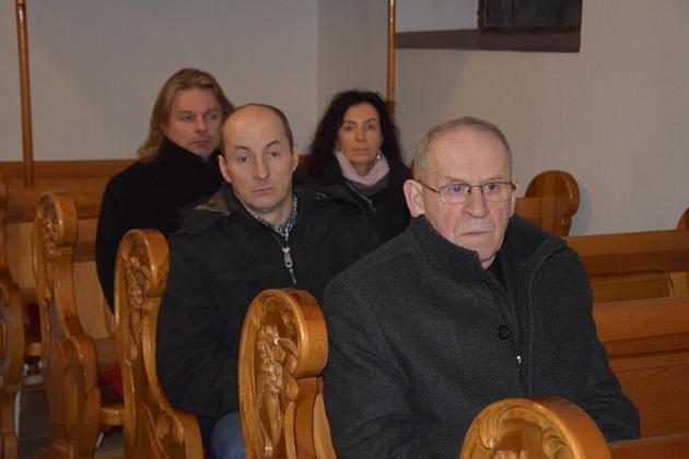 Uczestnicy świątecznego spotkania Gminnego Koła Pszczelarzy siedzą na drewnianych ławkach.