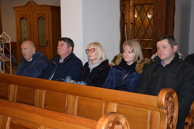Członkowie koła pszczelarzy siedzą w ławce podczas świątecznego spotkania.
