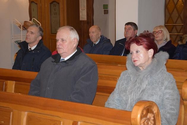 Członkowie Gminnego Koła Pszczelarzy siedzą w ławkach podczas świątecznego spotkania.