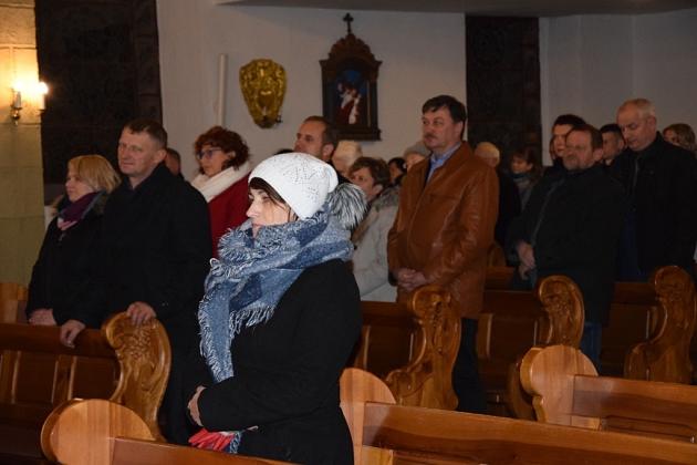 Uczestnicy świątecznego spotkania pszczelarzy w sali z ławkami, widoczne dekoracje na ścianach.
