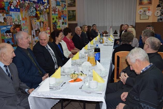 Uczestnicy świątecznego spotkania pszczelarzy siedzą przy stole.