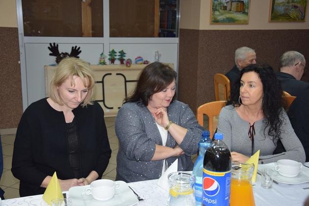 Trzy kobiety siedzą przy stole, rozmawiając na świątecznym spotkaniu pszczelarzy.