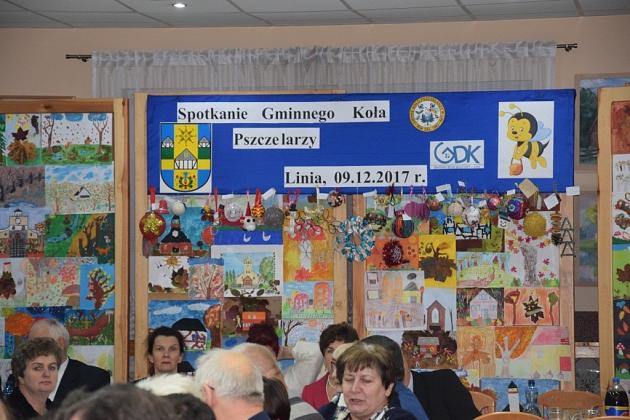 Świąteczne spotkanie pszczelarzy z dekorowanym tłem i siedzącymi uczestnikami.