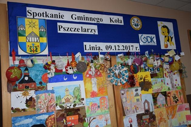Niebieska tablica Koła Pszczelarzy ozdobiona barwnymi świątecznymi pracami dziecięcymi.
