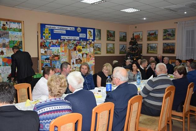 Grupa pszczelarzy spotyka się przy stołach na świątecznym spotkaniu.