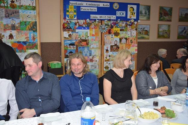 Uczestnicy świątecznego spotkania Gminnego Koła Pszczelarzy siedzą przy stole.