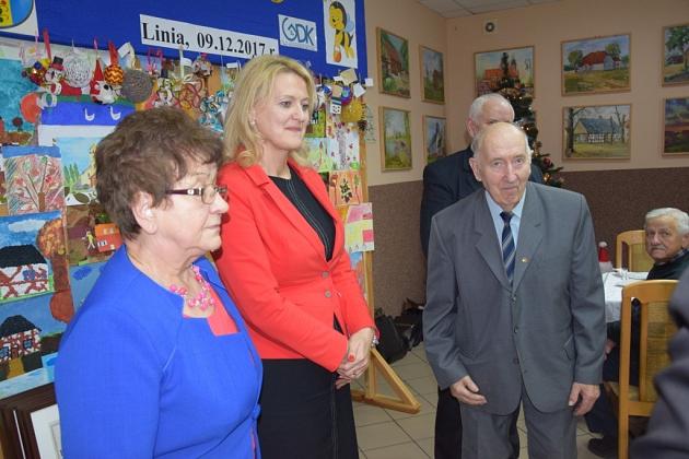 Trzy osoby, w tym dwie kobiety i starszy mężczyzna, stoją na świątecznym spotkaniu pszczelarzy.
