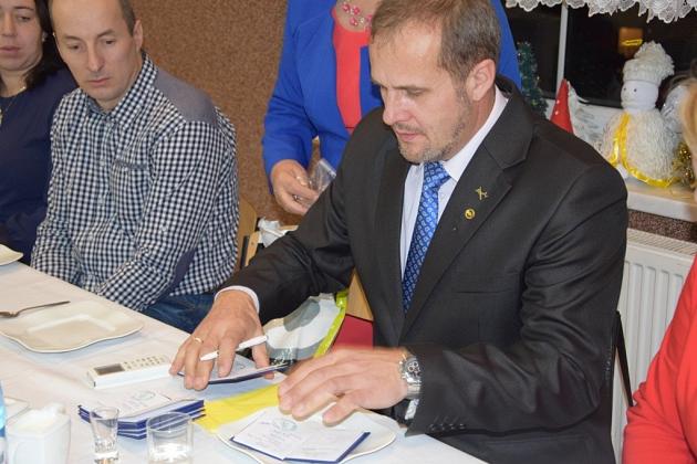 Mężczyzna w garniturze podpisuje dokumenty podczas spotkania pszczelarzy.