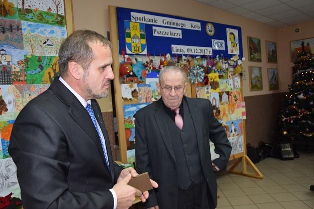 Mężczyźni w garniturach dyskutują na świątecznym spotkaniu, jeden trzyma upominek.