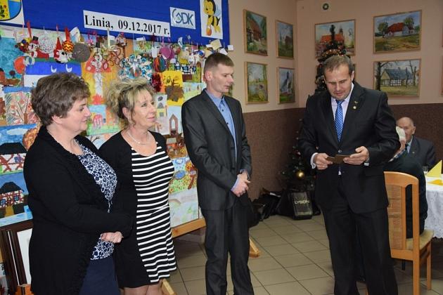 Cztery osoby na spotkaniu pszczelarzy, mężczyzna w garniturze coś prezentuje.