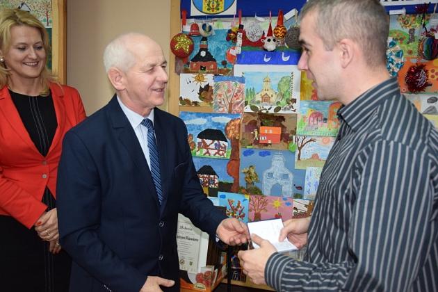 Starszy mężczyzna wręcza upominek młodszemu na spotkaniu Gminnego Koła Pszczelarzy.