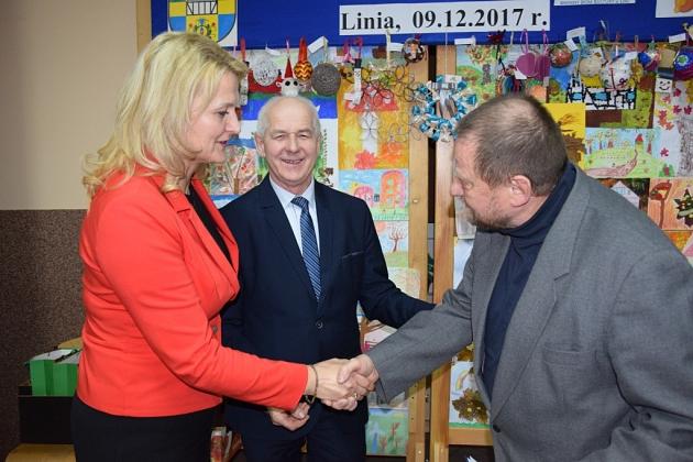 Uścisk dłoni na tle świątecznego spotkania Gminnego Koła Pszczelarzy.