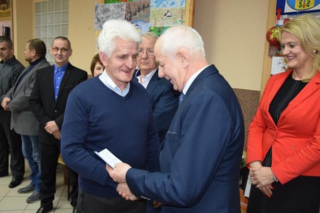 Starszy mężczyzna wręcza dokumenty młodszemu na świątecznym spotkaniu pszczelarzy.