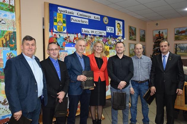 Grupa osób, w tym kobieta z nagrodą, pozuje podczas świątecznego spotkania pszczelarzy.