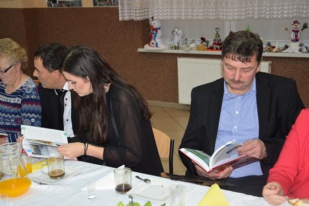 Pszczelarze na spotkaniu, siedzą przy stole i przeglądają książki.