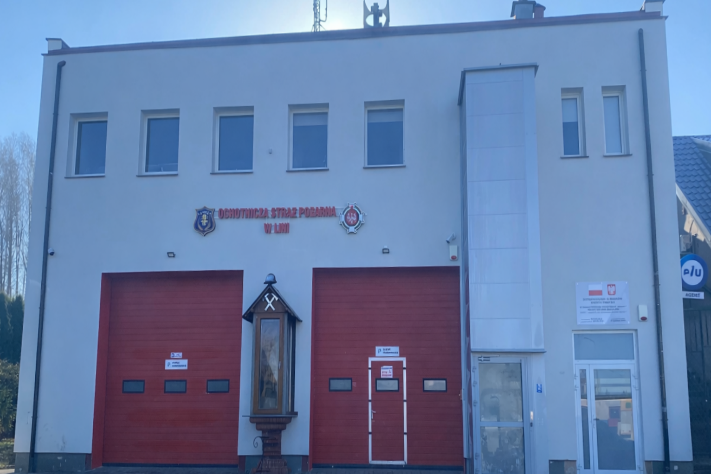 Remiza OSP Linia z dwoma czerwonymi bramami garażowymi i figurą.